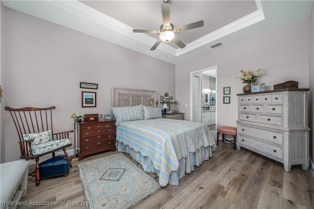 bedroom featuring ensuite bath, hardwood / wood-style flooring, ceiling fan, a tray ceiling, and ornamental molding