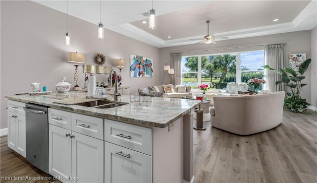 kitchen with sink, dishwasher, white cabinetry, a center island with sink, and a raised ceiling