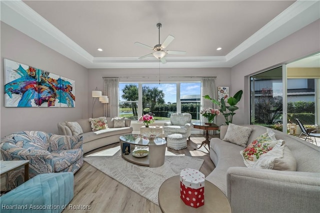 living room with ceiling fan, ornamental molding, a raised ceiling, and light hardwood / wood-style flooring