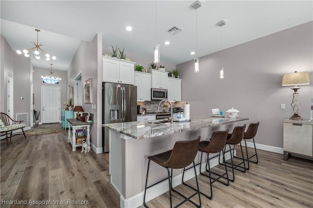 kitchen with a breakfast bar area, white cabinets, a chandelier, hanging light fixtures, and stainless steel appliances