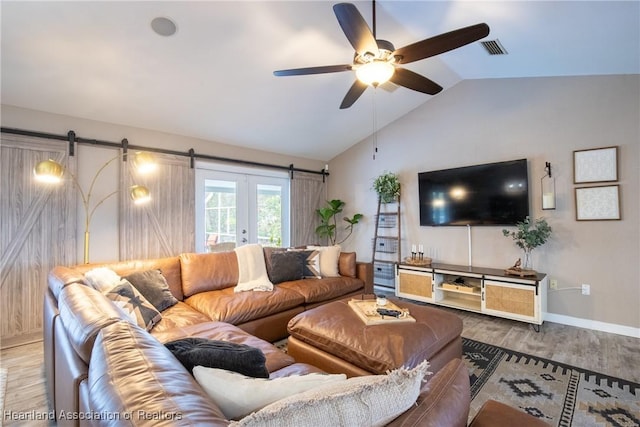 living room featuring a barn door, visible vents, ceiling fan, wood finished floors, and vaulted ceiling