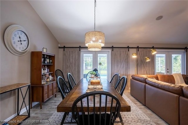 dining area featuring a wealth of natural light, vaulted ceiling, light wood finished floors, and a barn door