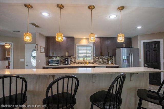 kitchen with visible vents, decorative backsplash, light countertops, stainless steel refrigerator with ice dispenser, and a sink