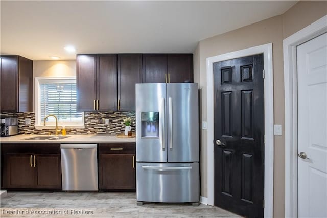 kitchen featuring dark brown cabinetry, decorative backsplash, stainless steel appliances, light countertops, and a sink