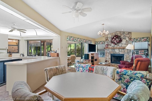 dining area with a stone fireplace, ceiling fan with notable chandelier, and vaulted ceiling