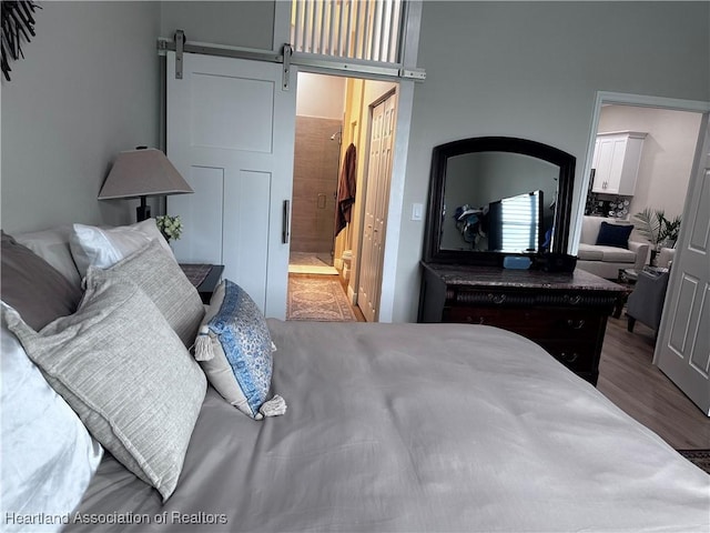 bedroom featuring a barn door, a closet, ensuite bath, and wood-type flooring