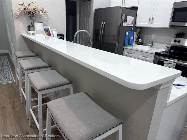 kitchen featuring a kitchen bar, appliances with stainless steel finishes, white cabinets, and hardwood / wood-style flooring