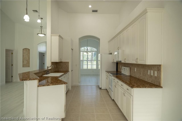 kitchen with white appliances, sink, dark stone countertops, decorative light fixtures, and kitchen peninsula