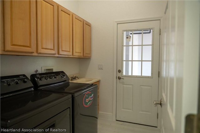 clothes washing area with cabinets, sink, washing machine and dryer, and light hardwood / wood-style flooring