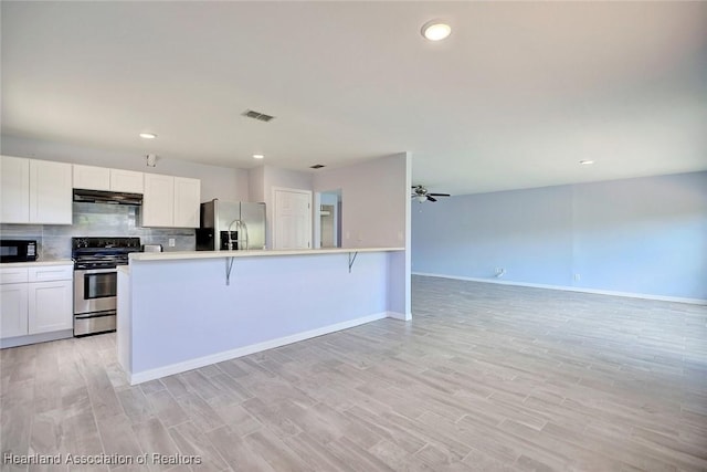 kitchen with light hardwood / wood-style floors, a breakfast bar, white cabinets, and appliances with stainless steel finishes