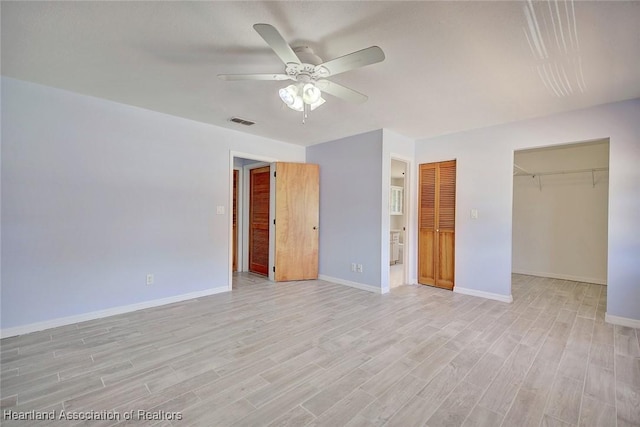 unfurnished bedroom featuring ceiling fan, light hardwood / wood-style floors, a spacious closet, and a closet