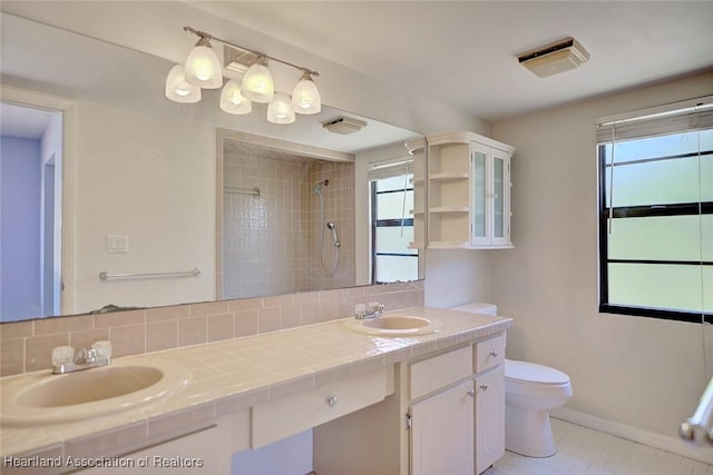 bathroom with tile patterned floors, vanity, tasteful backsplash, toilet, and a tile shower