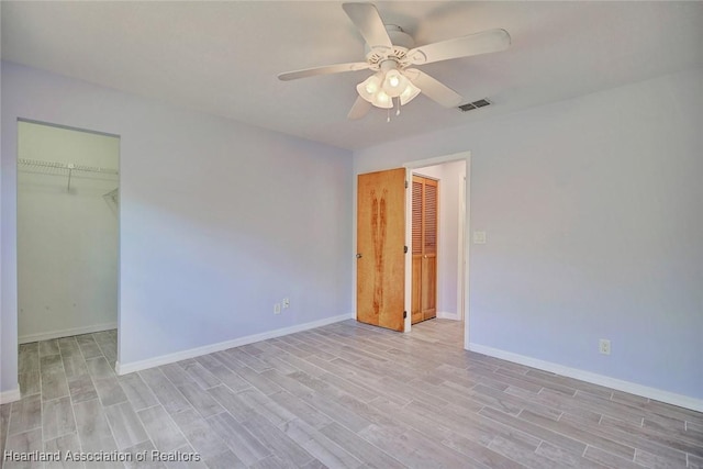 unfurnished bedroom with light wood-type flooring, ceiling fan, a spacious closet, and a closet