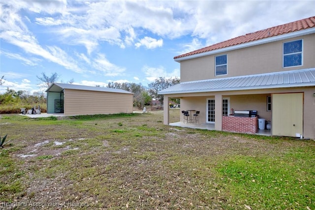 rear view of property featuring a yard, an outdoor structure, and a patio