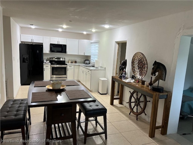 kitchen with white cabinetry, sink, light tile patterned floors, and black appliances