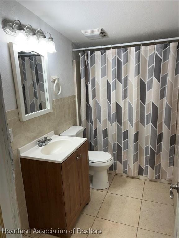 bathroom with walk in shower, toilet, tile walls, vanity, and tile patterned flooring