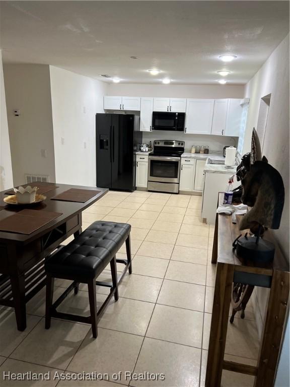 kitchen featuring white cabinetry, light tile patterned flooring, and black appliances