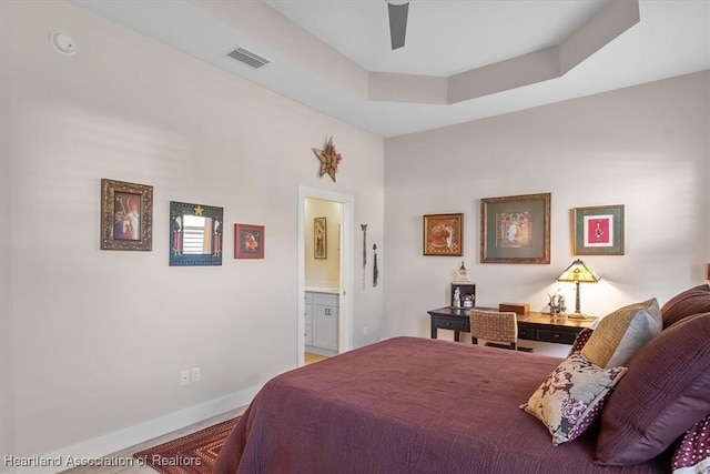 bedroom featuring a raised ceiling, ceiling fan, and ensuite bath