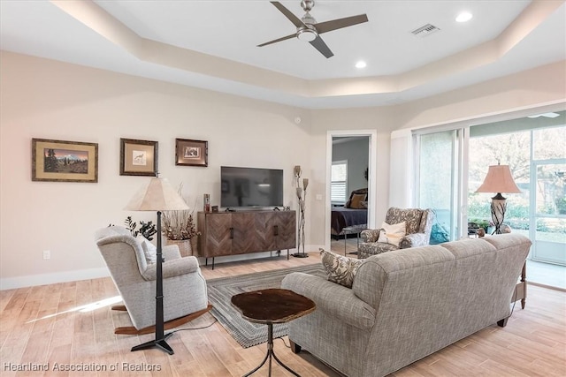 living room featuring a tray ceiling, light hardwood / wood-style flooring, and ceiling fan