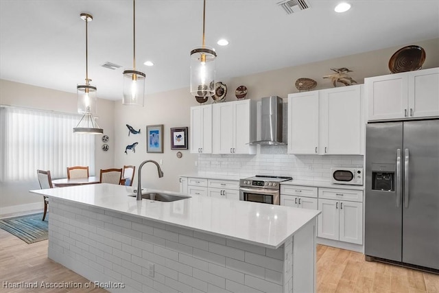 kitchen featuring appliances with stainless steel finishes, decorative light fixtures, sink, and wall chimney exhaust hood