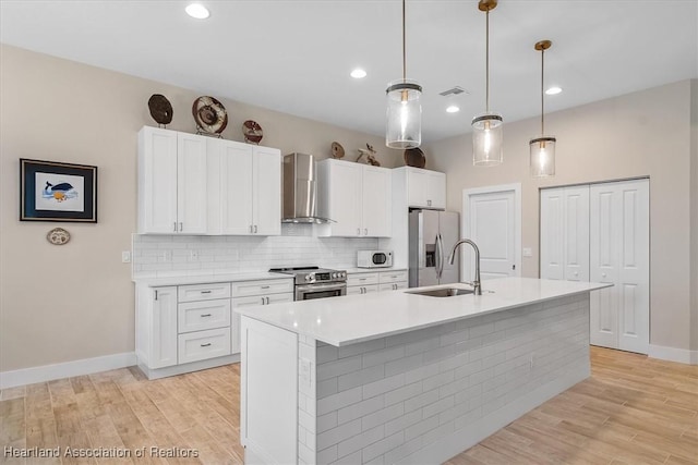 kitchen featuring a kitchen island with sink, hanging light fixtures, white cabinetry, stainless steel appliances, and wall chimney exhaust hood