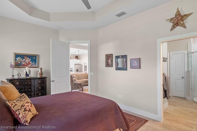 bedroom with stainless steel refrigerator with ice dispenser, ceiling fan, a raised ceiling, and light hardwood / wood-style floors