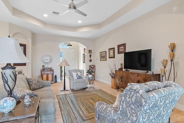 living room featuring a raised ceiling, ceiling fan, and light hardwood / wood-style floors