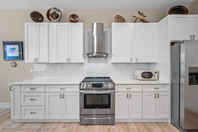 kitchen featuring stainless steel appliances, tasteful backsplash, white cabinets, wall chimney exhaust hood, and light wood-type flooring