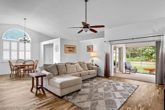 living room with ceiling fan with notable chandelier, light hardwood / wood-style flooring, and vaulted ceiling