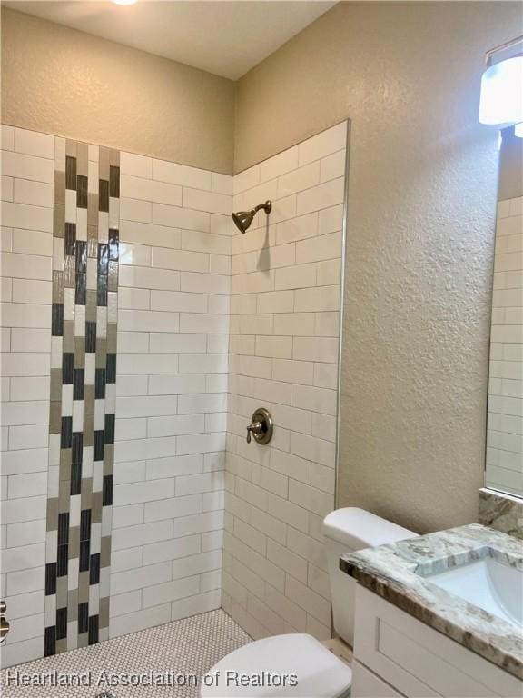 bathroom featuring a tile shower, vanity, and toilet