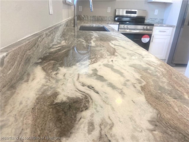 interior details featuring white cabinets, appliances with stainless steel finishes, light stone countertops, and sink