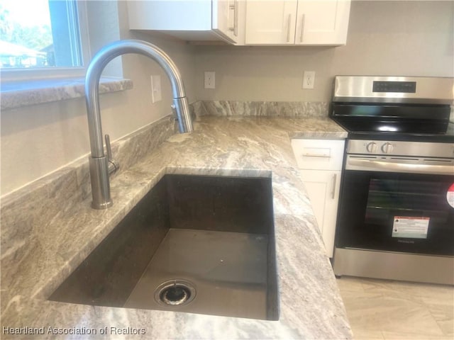 details featuring light stone countertops, stainless steel stove, white cabinetry, and sink