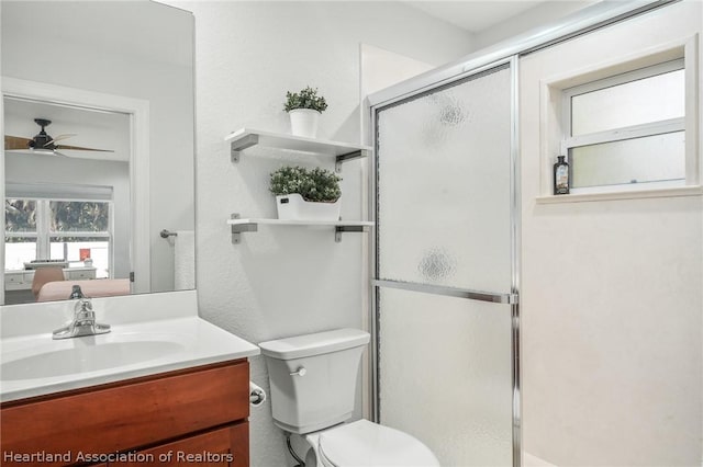 bathroom with walk in shower, ceiling fan, vanity, and toilet