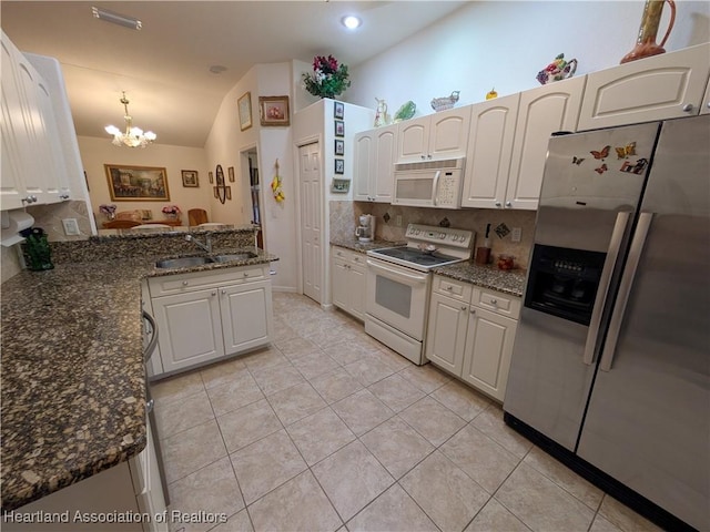 kitchen with white appliances, sink, vaulted ceiling, decorative light fixtures, and white cabinetry