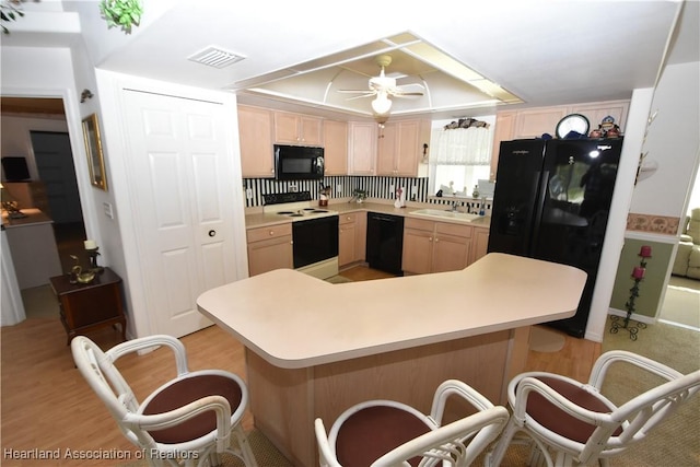 kitchen with ceiling fan, light wood-type flooring, kitchen peninsula, light brown cabinetry, and black appliances