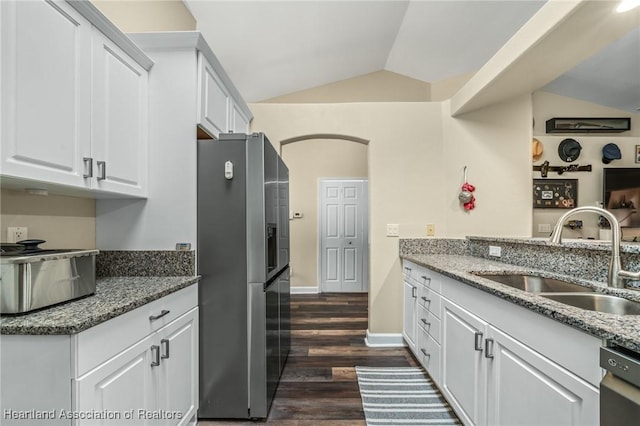 kitchen featuring stone counters, sink, stainless steel fridge, lofted ceiling, and white cabinets