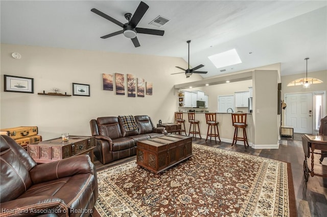 living room with vaulted ceiling with skylight, ceiling fan, and dark wood-type flooring