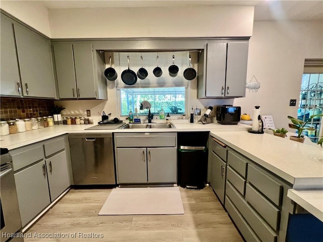 kitchen with tasteful backsplash, light countertops, light wood-style floors, a sink, and dishwasher