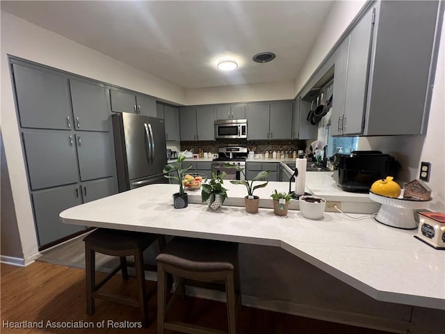 kitchen featuring gray cabinetry, a breakfast bar, appliances with stainless steel finishes, dark hardwood / wood-style flooring, and kitchen peninsula