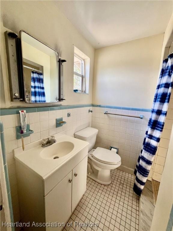 bathroom featuring a wainscoted wall, tile walls, toilet, vanity, and tile patterned floors