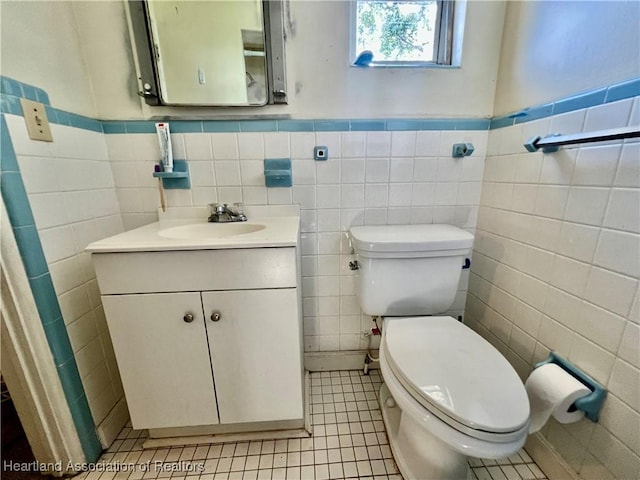 half bath featuring tile patterned flooring, a wainscoted wall, vanity, and toilet