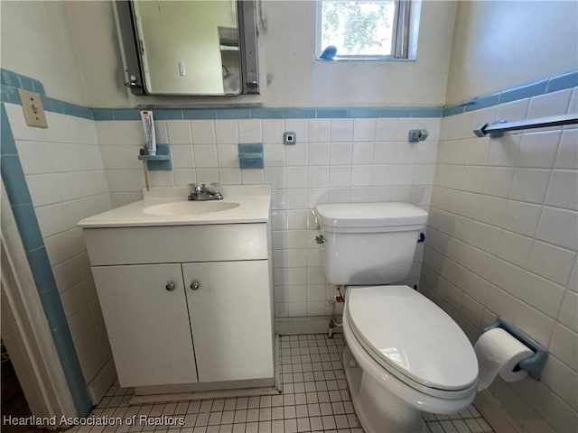 bathroom with toilet, vanity, tile patterned floors, and tile walls