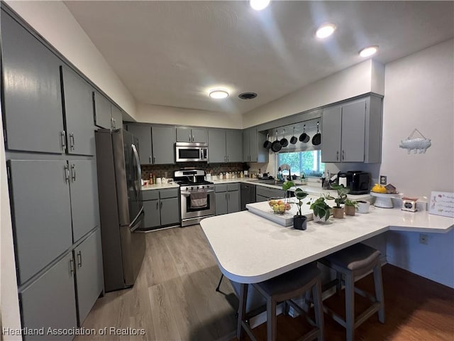 kitchen with kitchen peninsula, appliances with stainless steel finishes, decorative backsplash, a breakfast bar, and light hardwood / wood-style floors