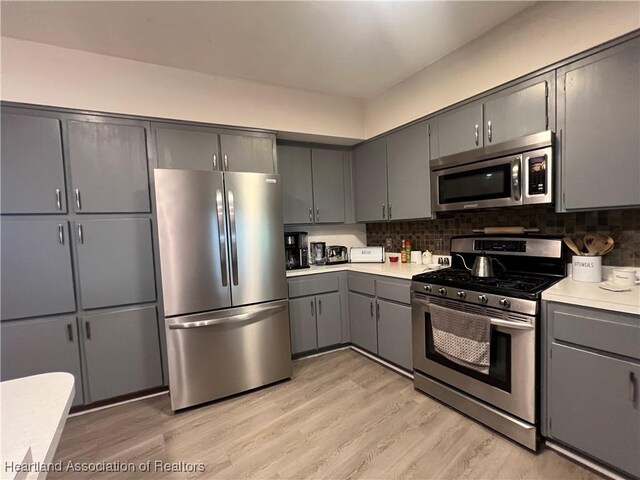 kitchen featuring kitchen peninsula, appliances with stainless steel finishes, a kitchen bar, gray cabinetry, and light hardwood / wood-style flooring