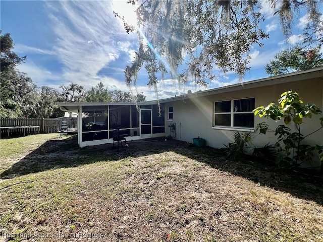 rear view of property featuring a sunroom, fence, a lawn, and stucco siding