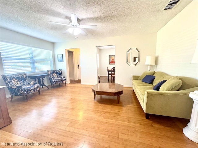 living room with ceiling fan, a textured ceiling, and light hardwood / wood-style flooring