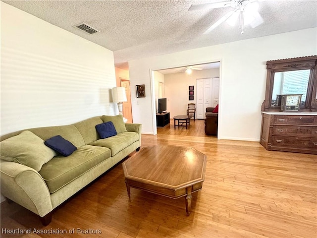 living room featuring ceiling fan, light hardwood / wood-style floors, and a textured ceiling