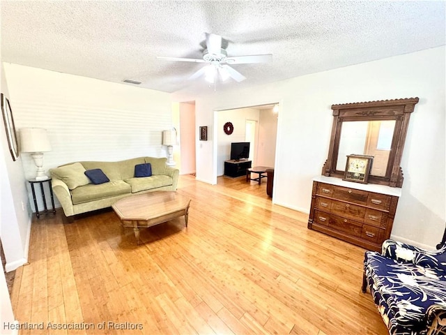 living room featuring ceiling fan, a textured ceiling, and light wood-type flooring