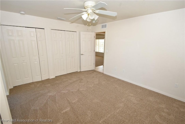 unfurnished bedroom with ceiling fan, carpet flooring, and two closets