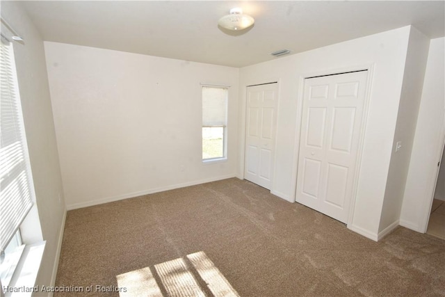 unfurnished bedroom featuring multiple closets and light carpet